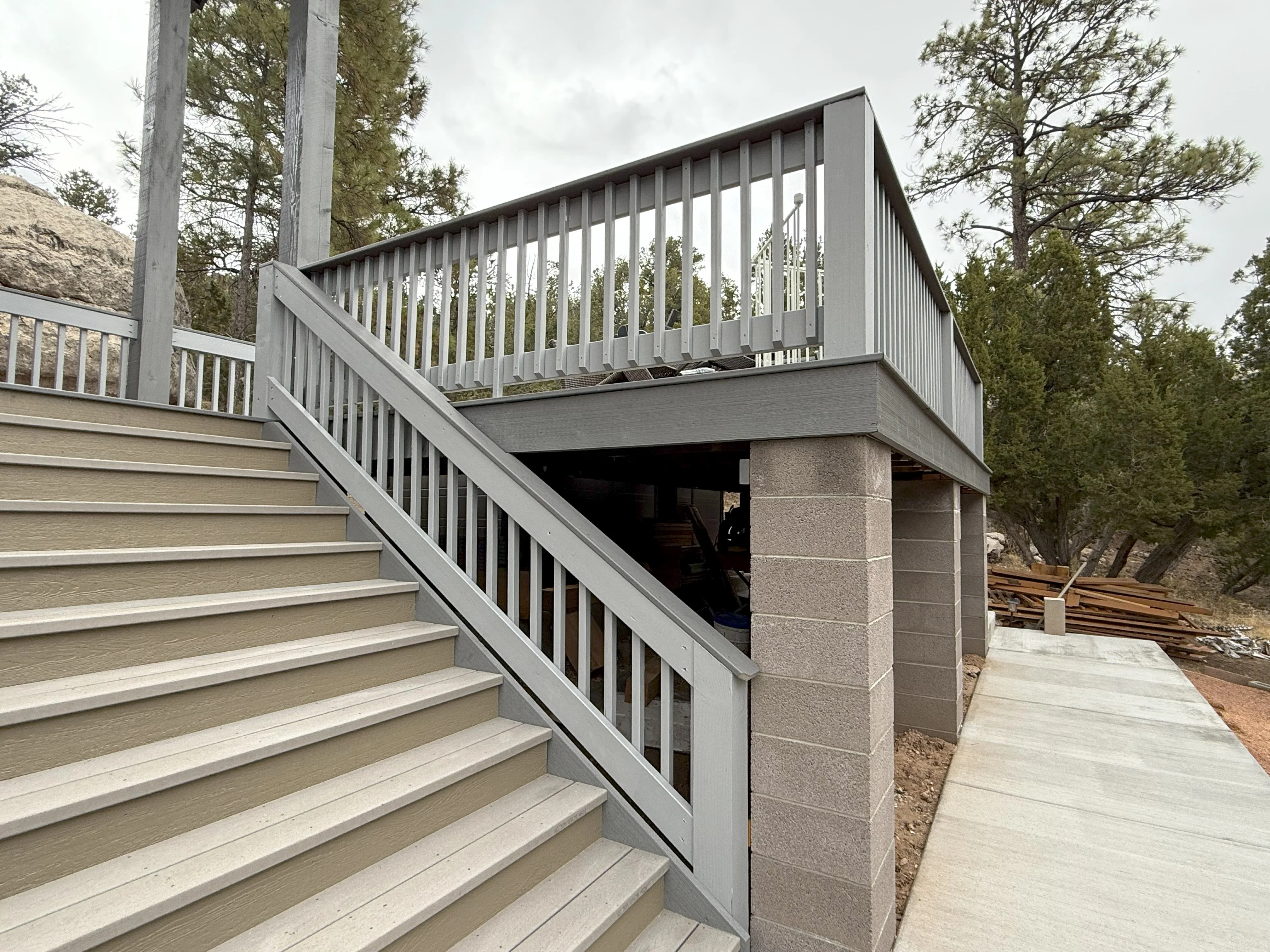 Gray and white composite deck with painted stairs, vertical spindle railings, and concrete support posts