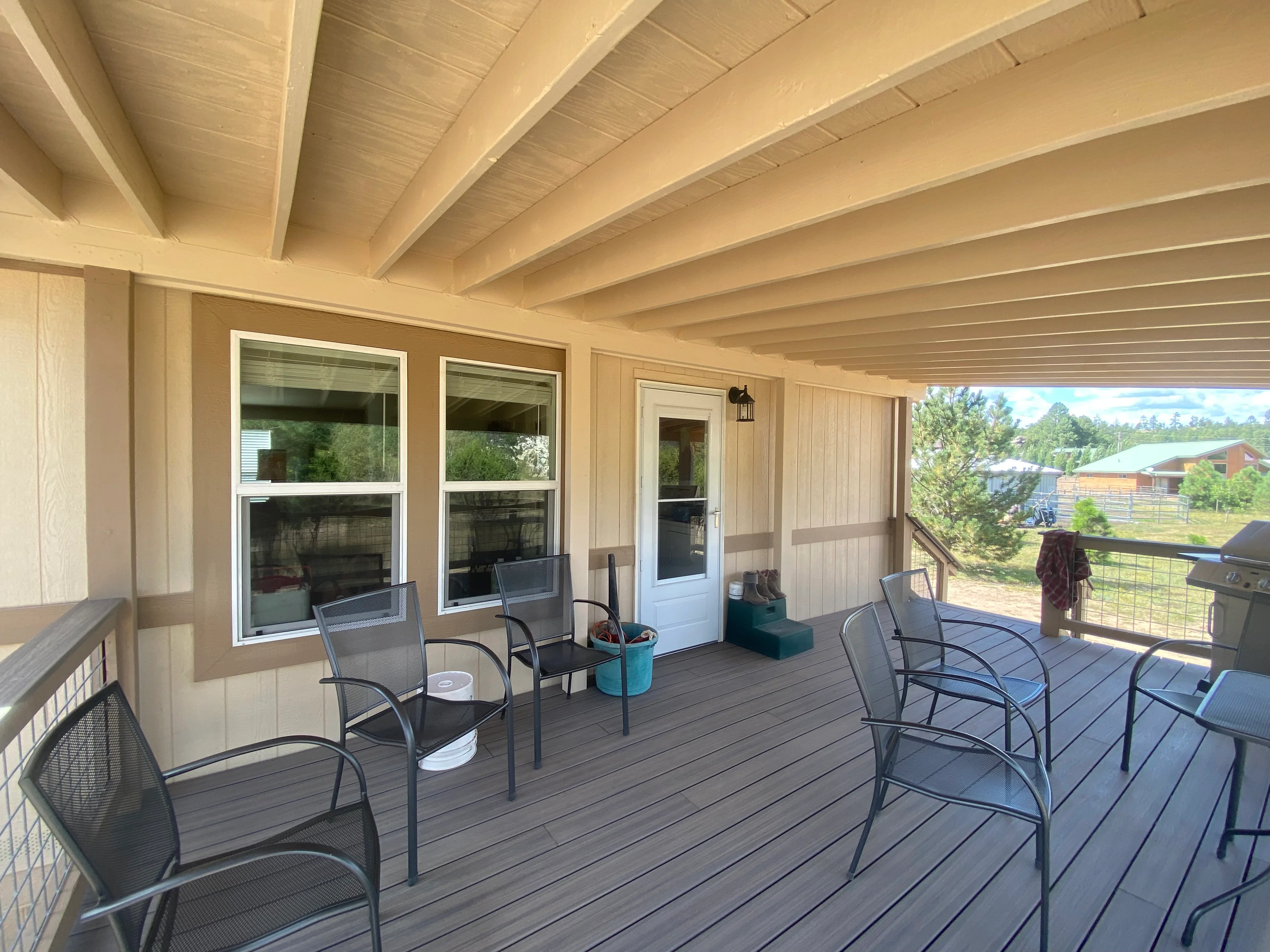 Cream and tan painted porch with white-trimmed windows, exposed beams, and dark gray stained deck