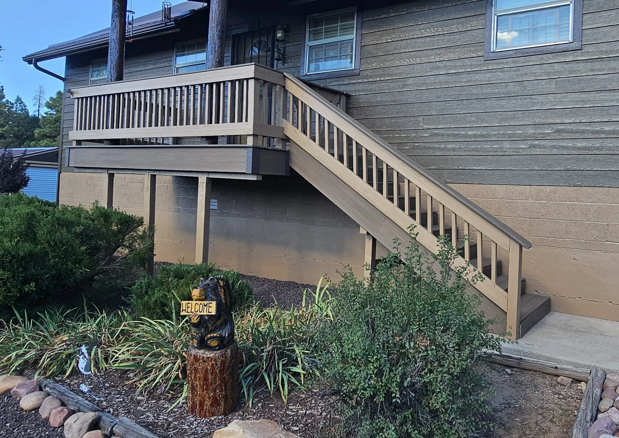 Stained composite deck with vertical railings and refreshed exterior siding on elevated home