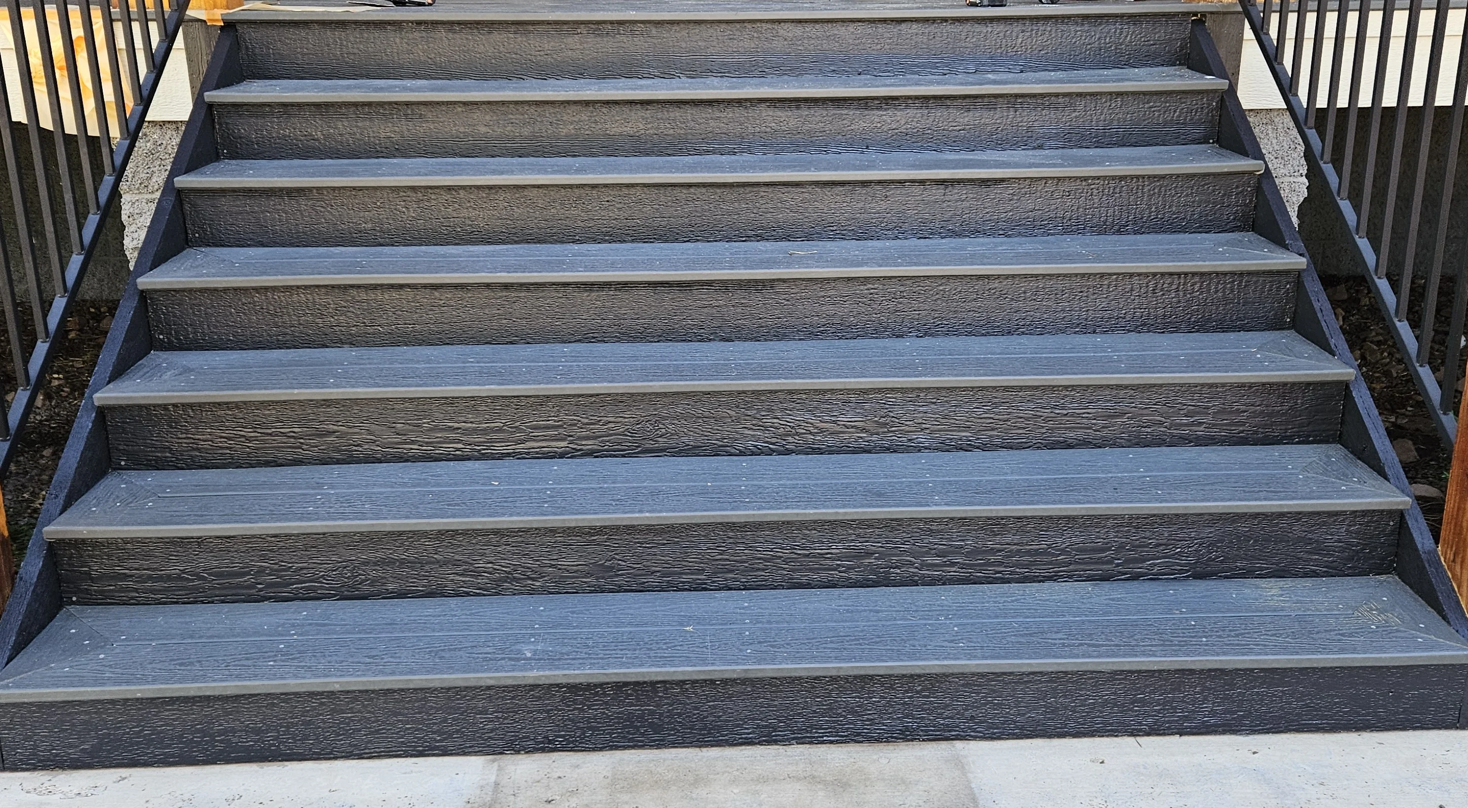 Exterior wooden stairs with dark charcoal risers and blue-gray stained treads, metal railings on both sides