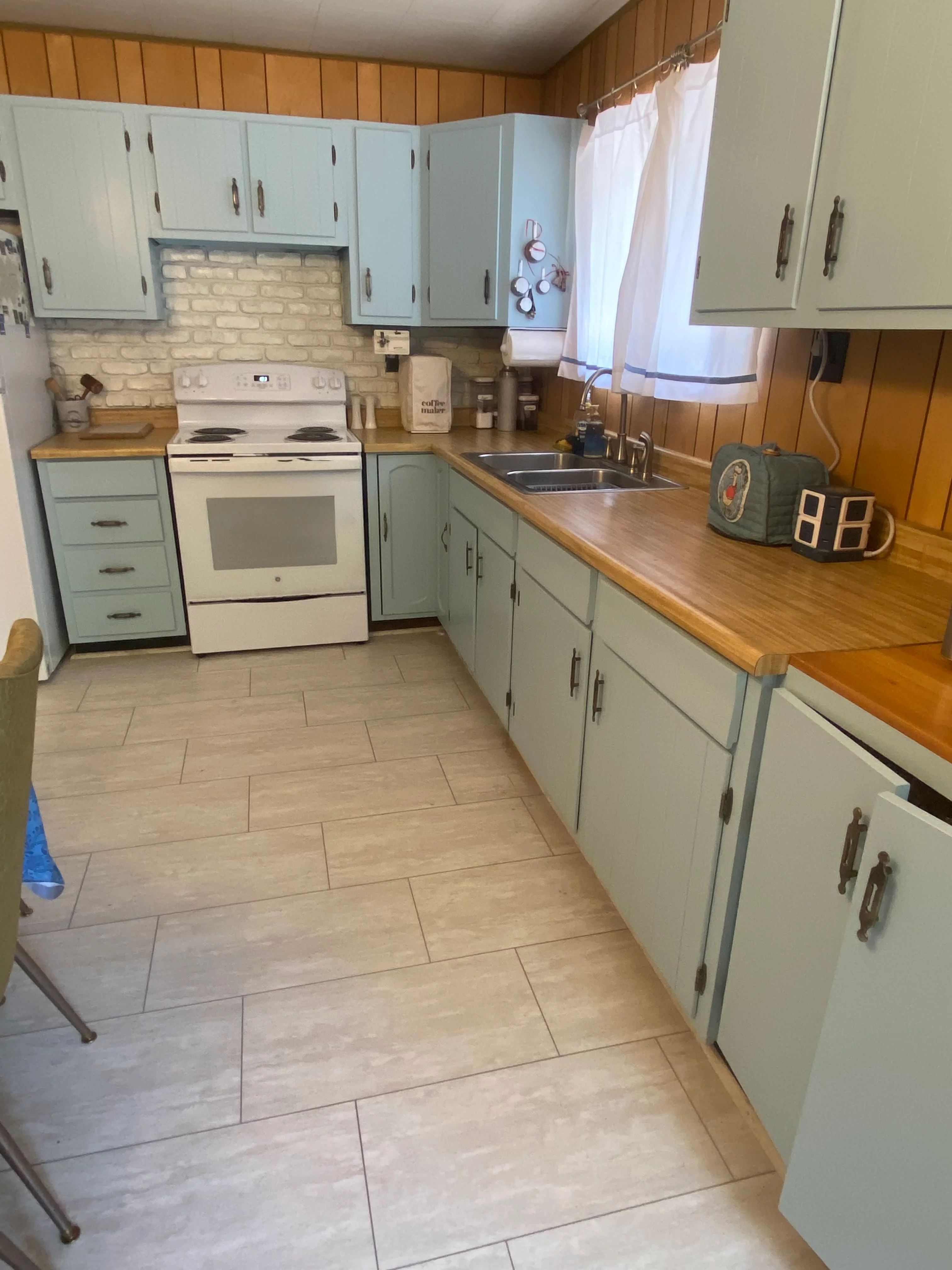 Blue-green painted kitchen cabinets with white subway tile backsplash and wood countertops