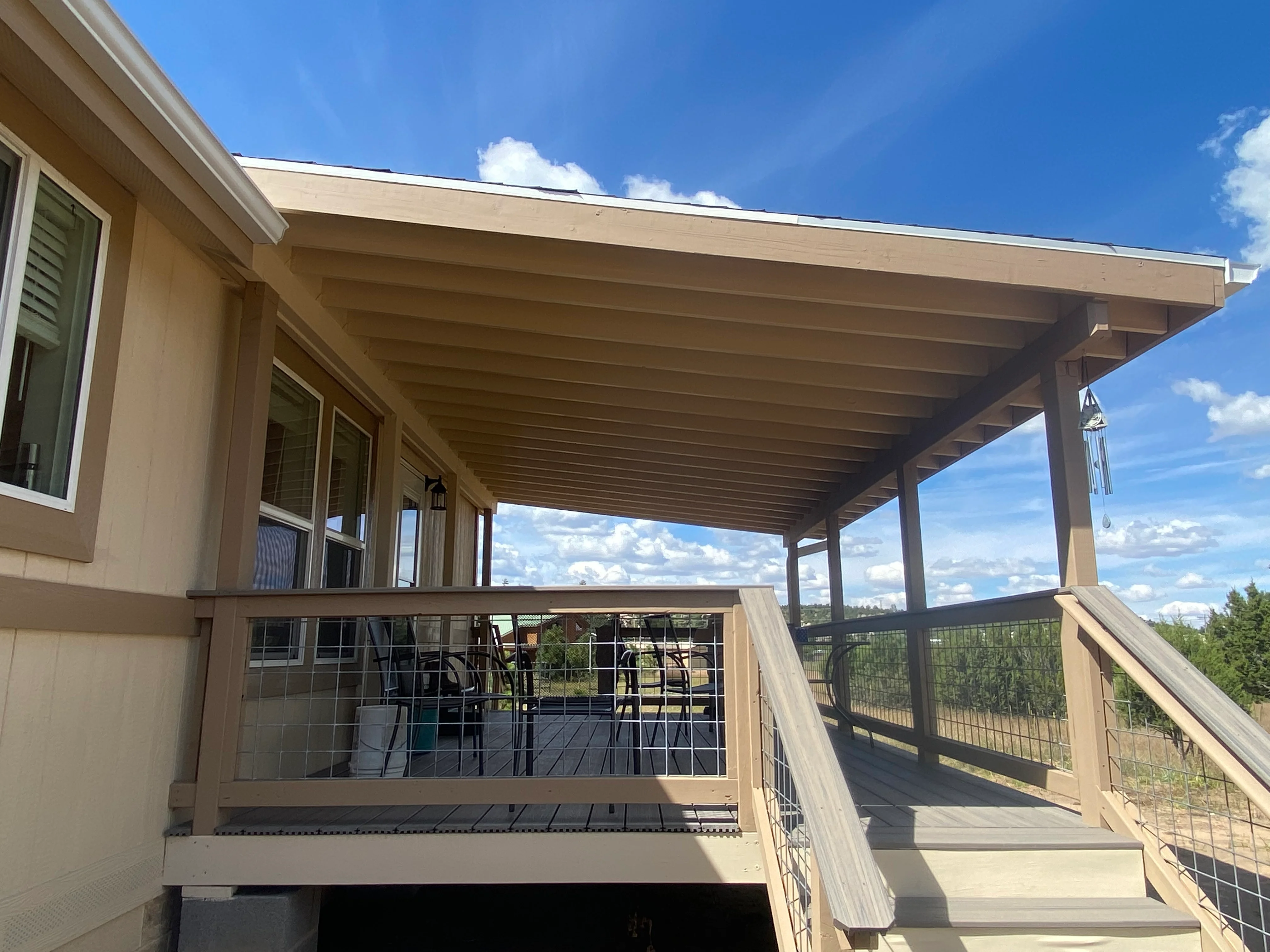 Elevated wood deck with stained posts, beams, and cable railings under covered patio structure