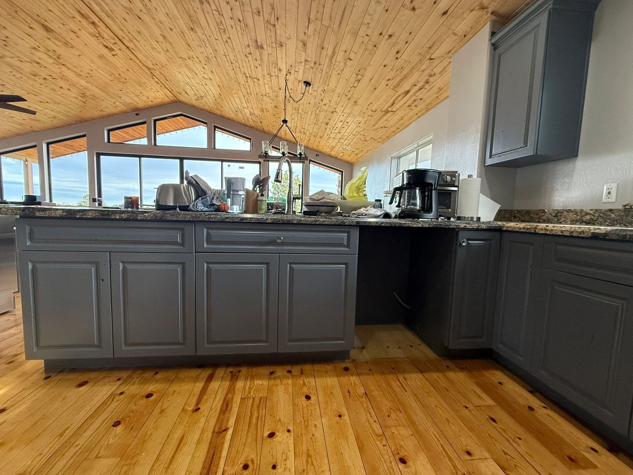 Gray painted kitchen cabinets with granite countertops and wood ceiling