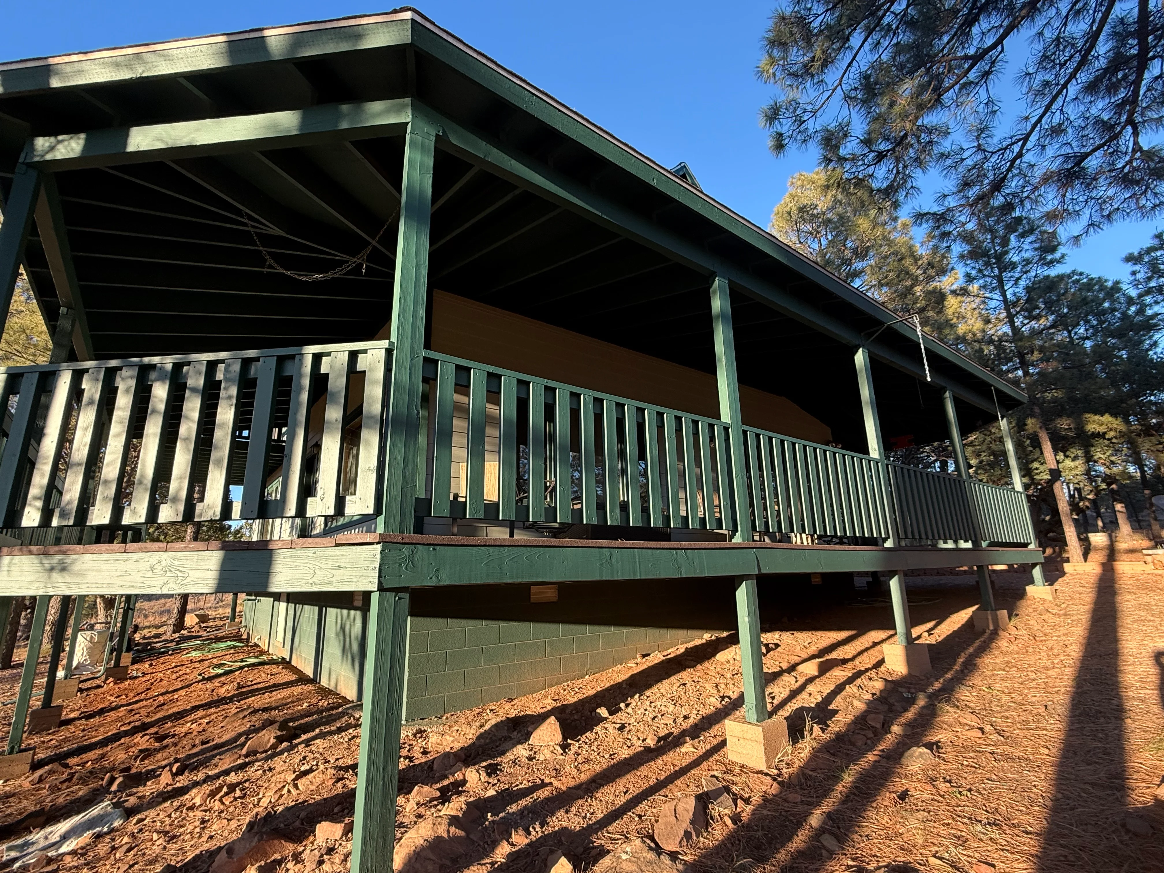 Green-stained wood deck with railings, posts, and fascia on elevated residential structure