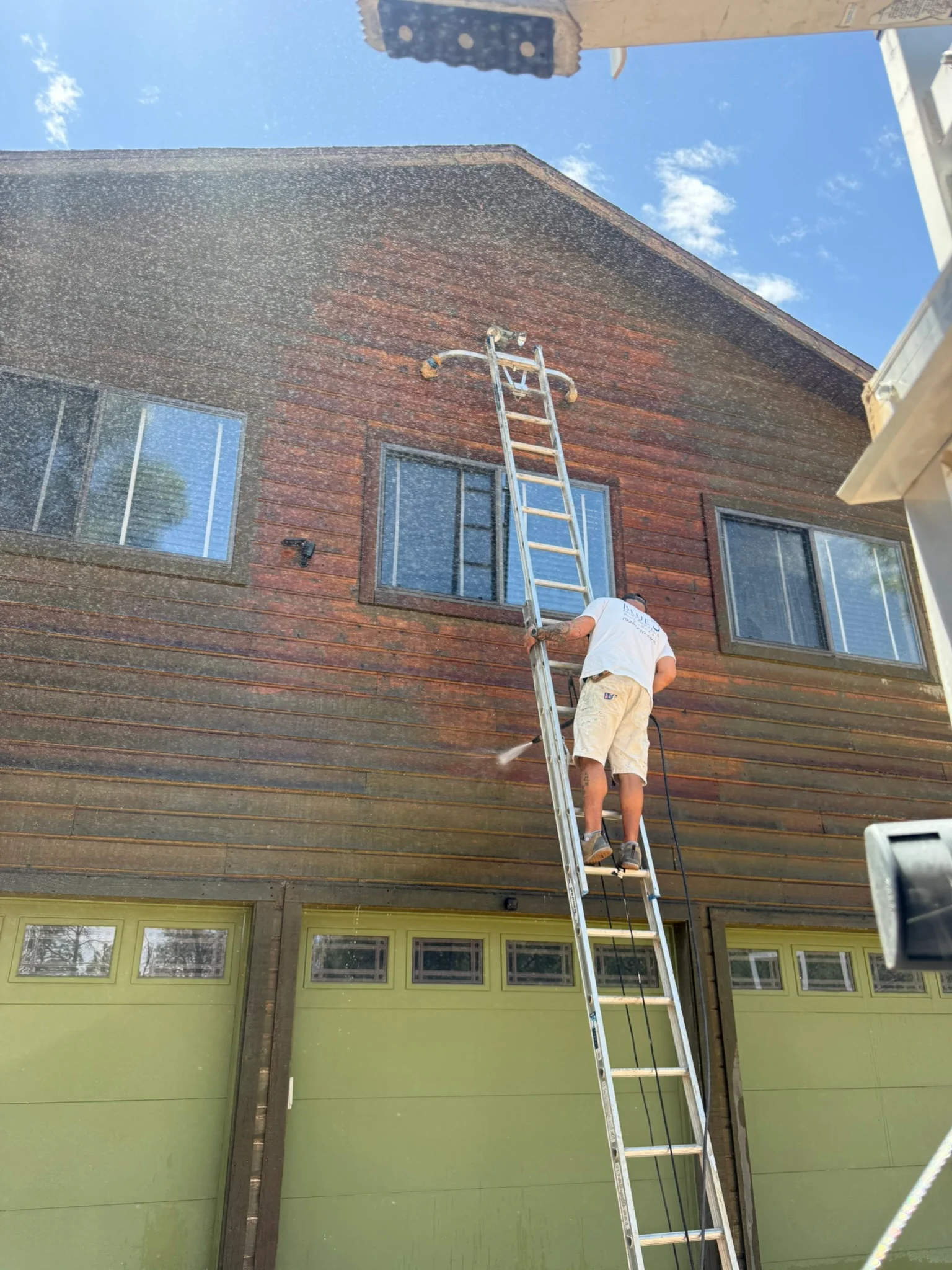 Worker on ladder staining weathered wood siding and trim on residential home exterior