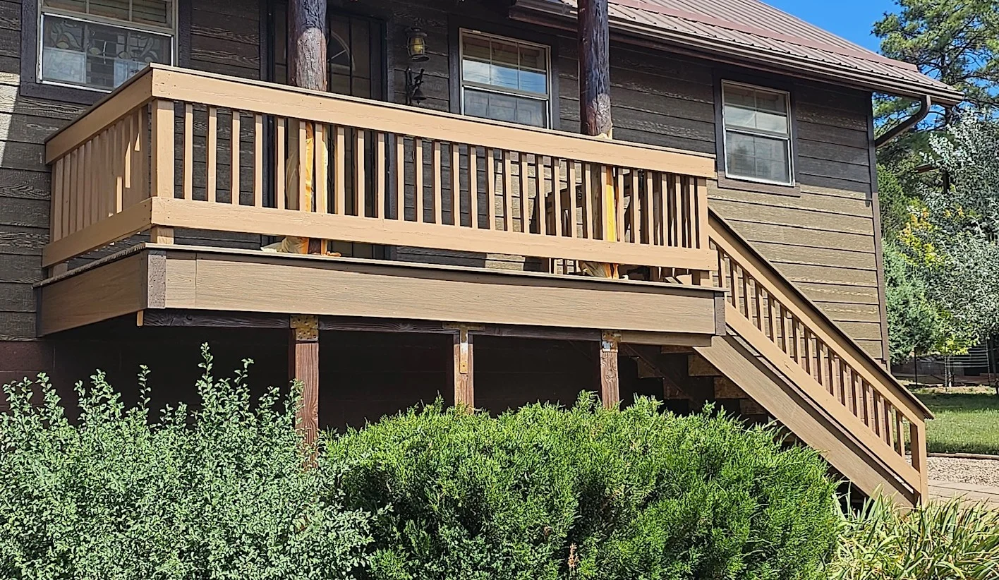 Two-tier wood deck with tan stain, vertical railings, and stairs attached to house