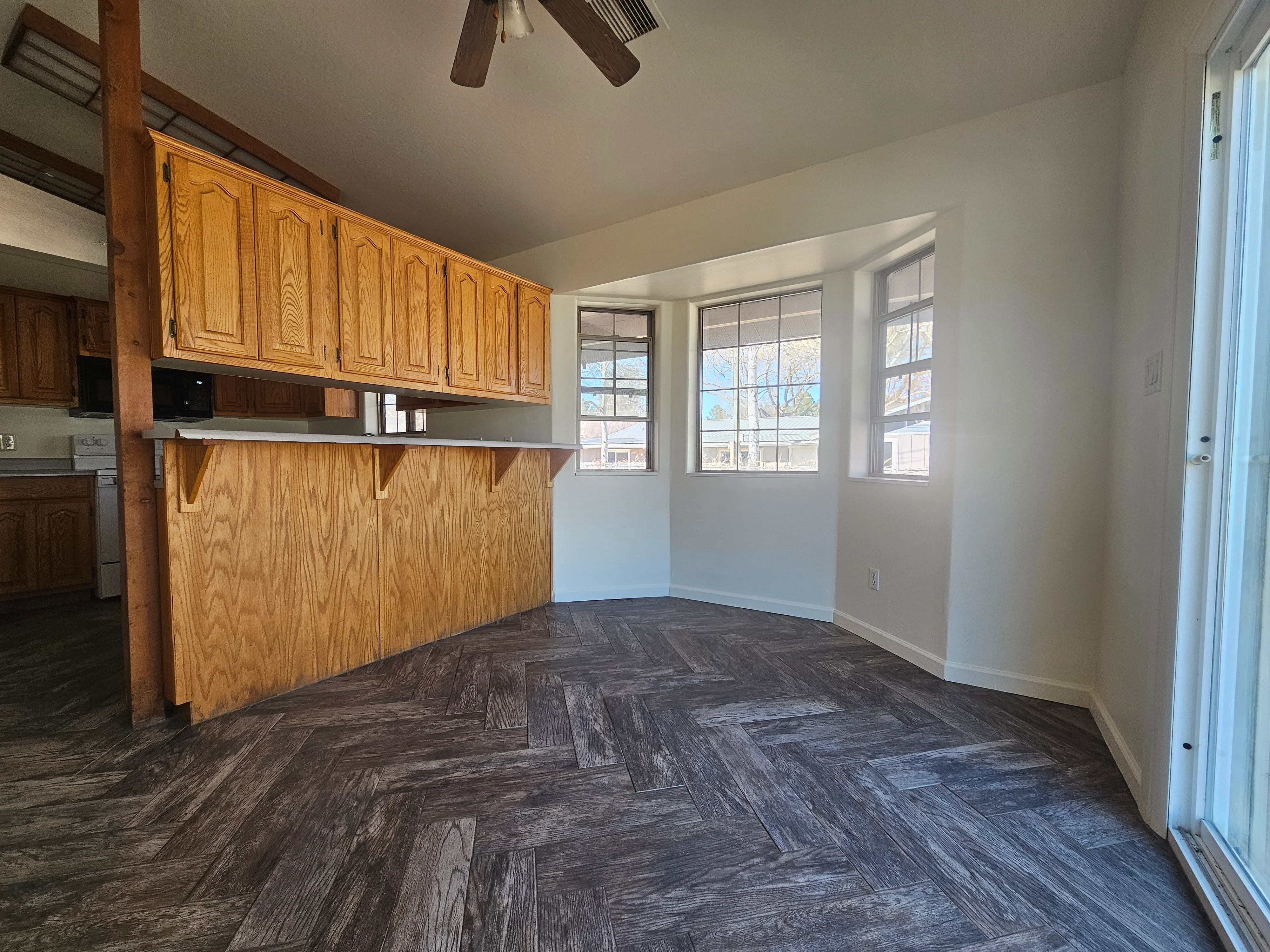 Interior kitchen and living room with painted drywall walls and ceiling, wood cabinets, herringbone flooring
