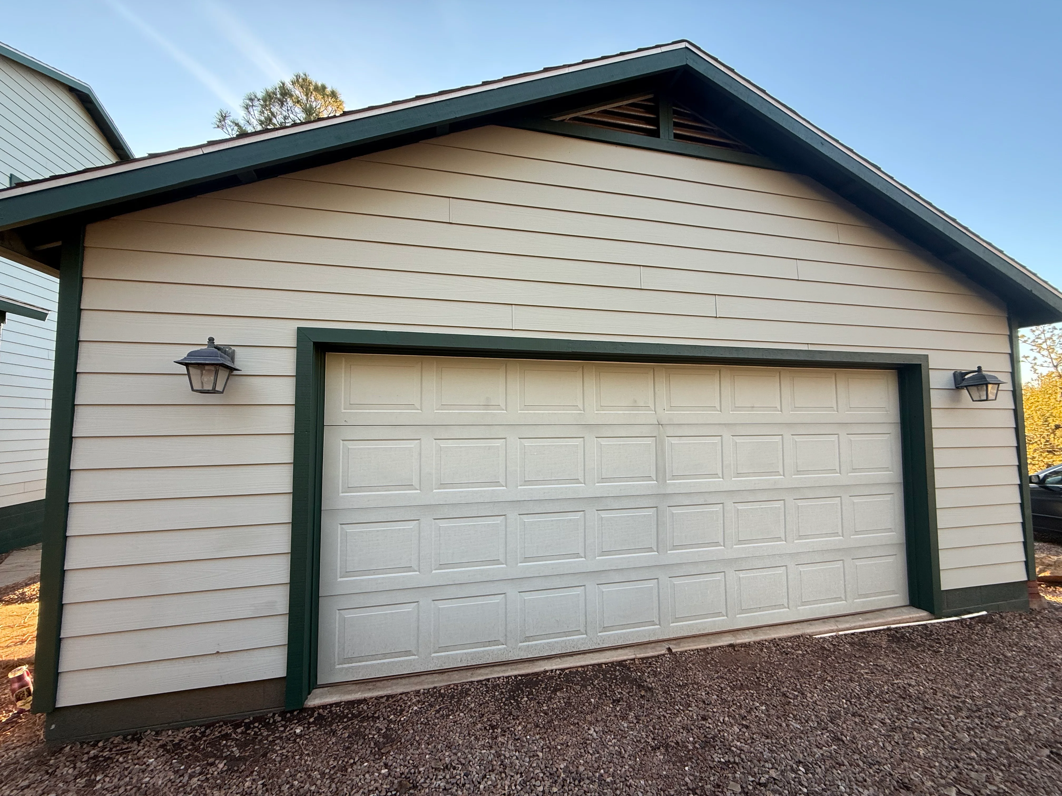 Newly painted garage with taupe siding, dark green trim, and white garage door