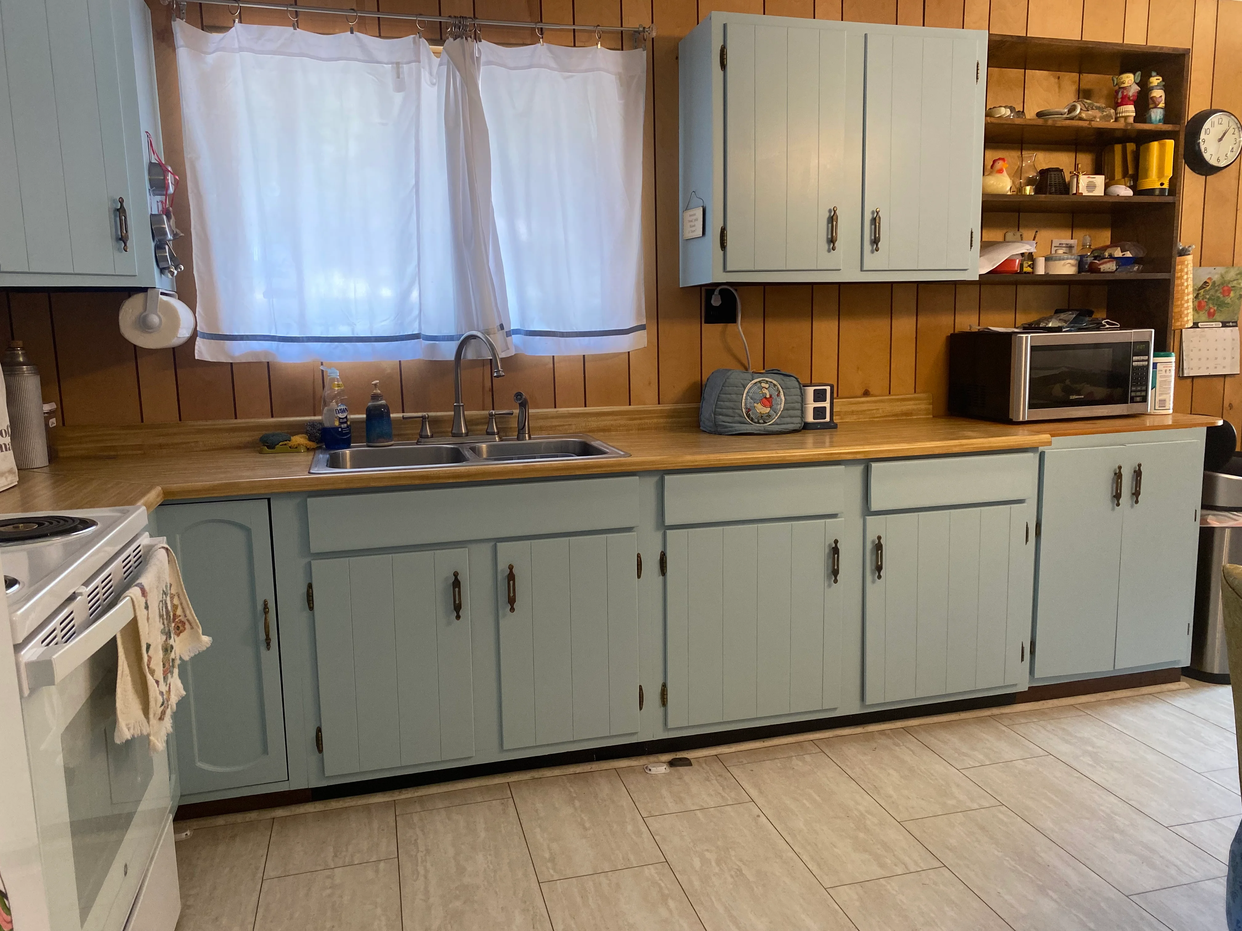 Sage-green painted kitchen cabinets with wood countertops and light gray upper cabinetry