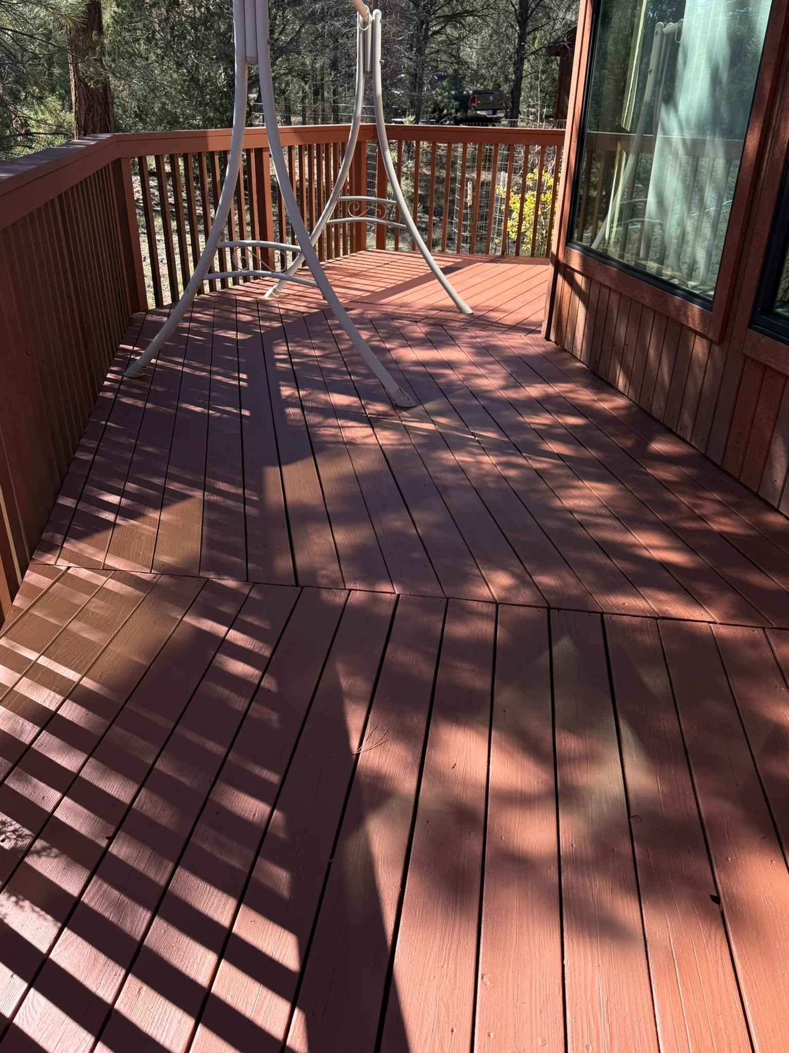 Stained wood deck with railings and trim overlooking forest landscape