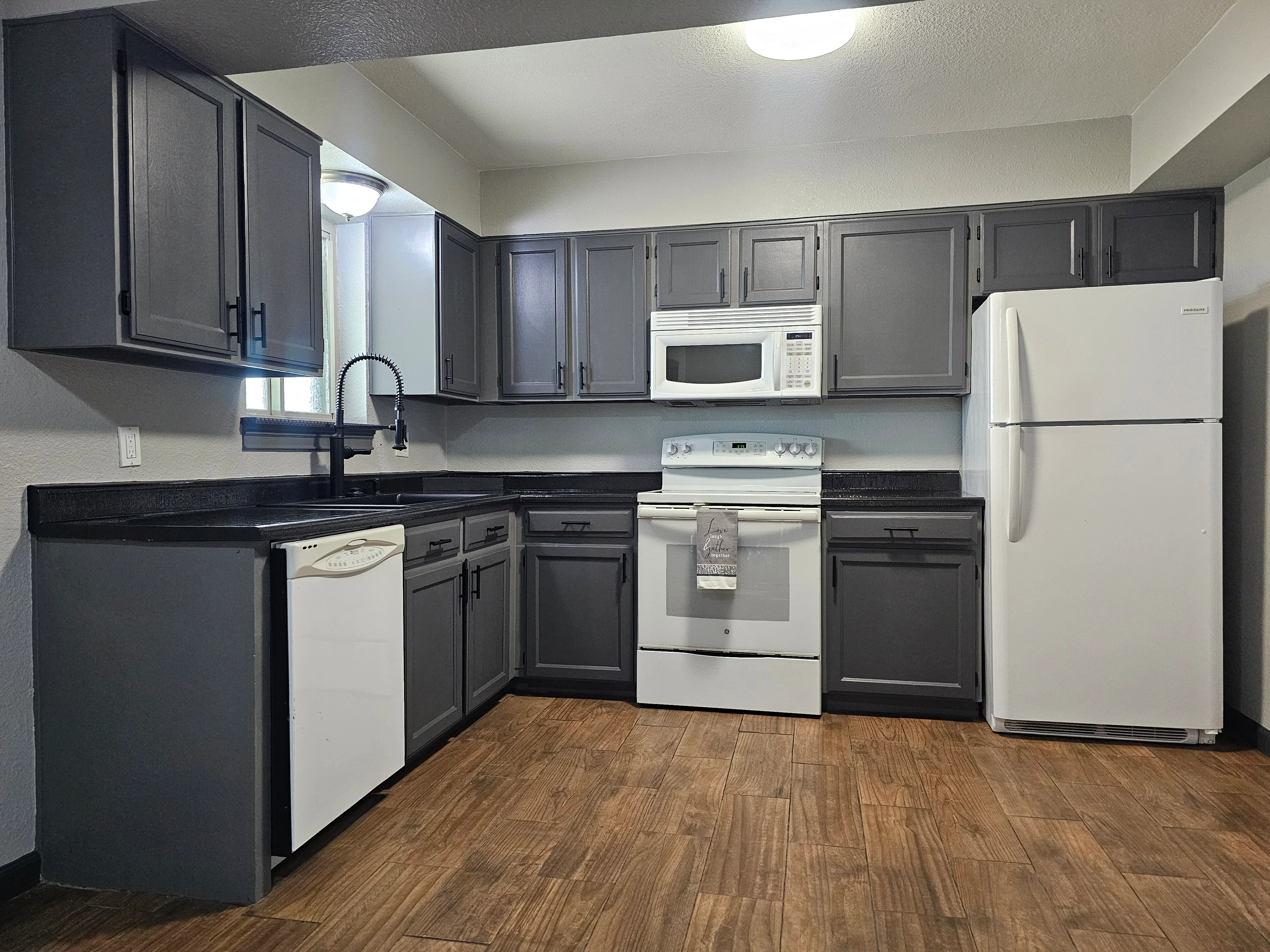 Dark gray painted kitchen cabinets with black granite countertops and wood flooring