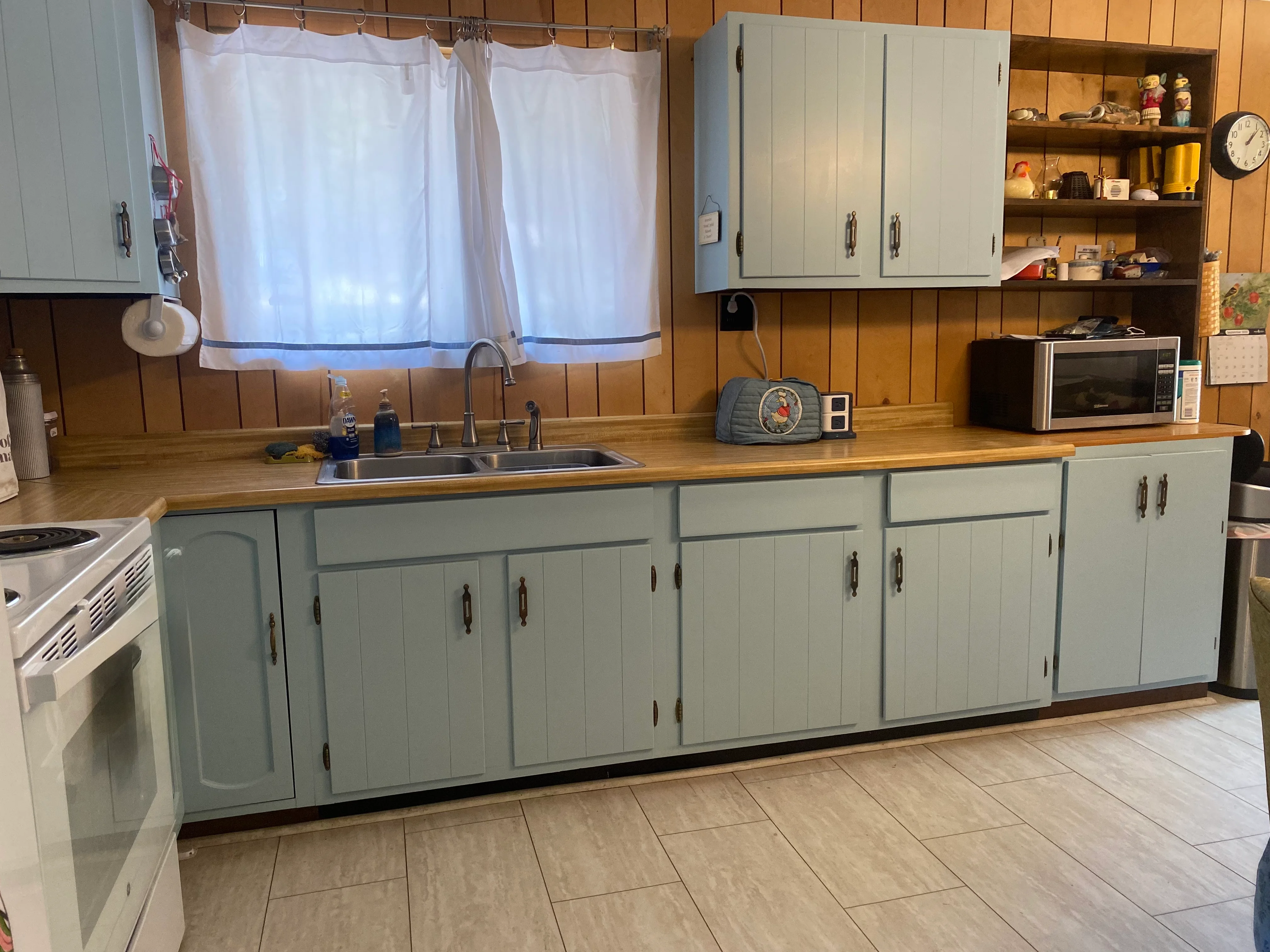 Sage green painted kitchen cabinets with hardware, wood countertop, and wood paneled walls