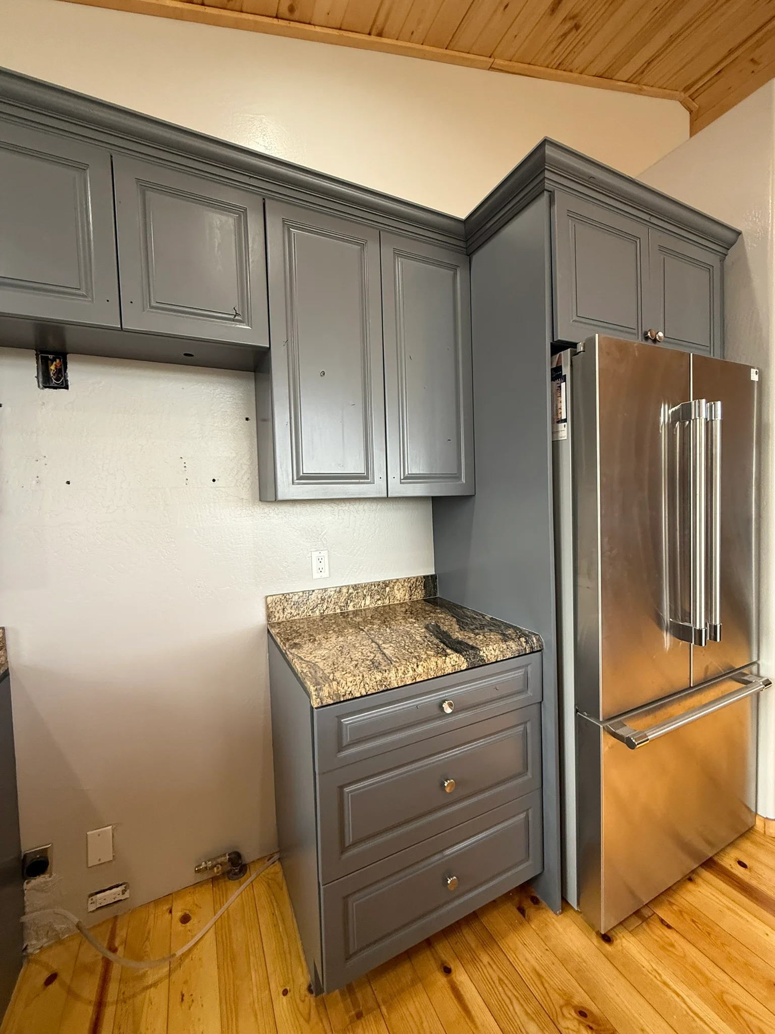 Gray painted kitchen cabinets with granite countertop and stainless steel refrigerator