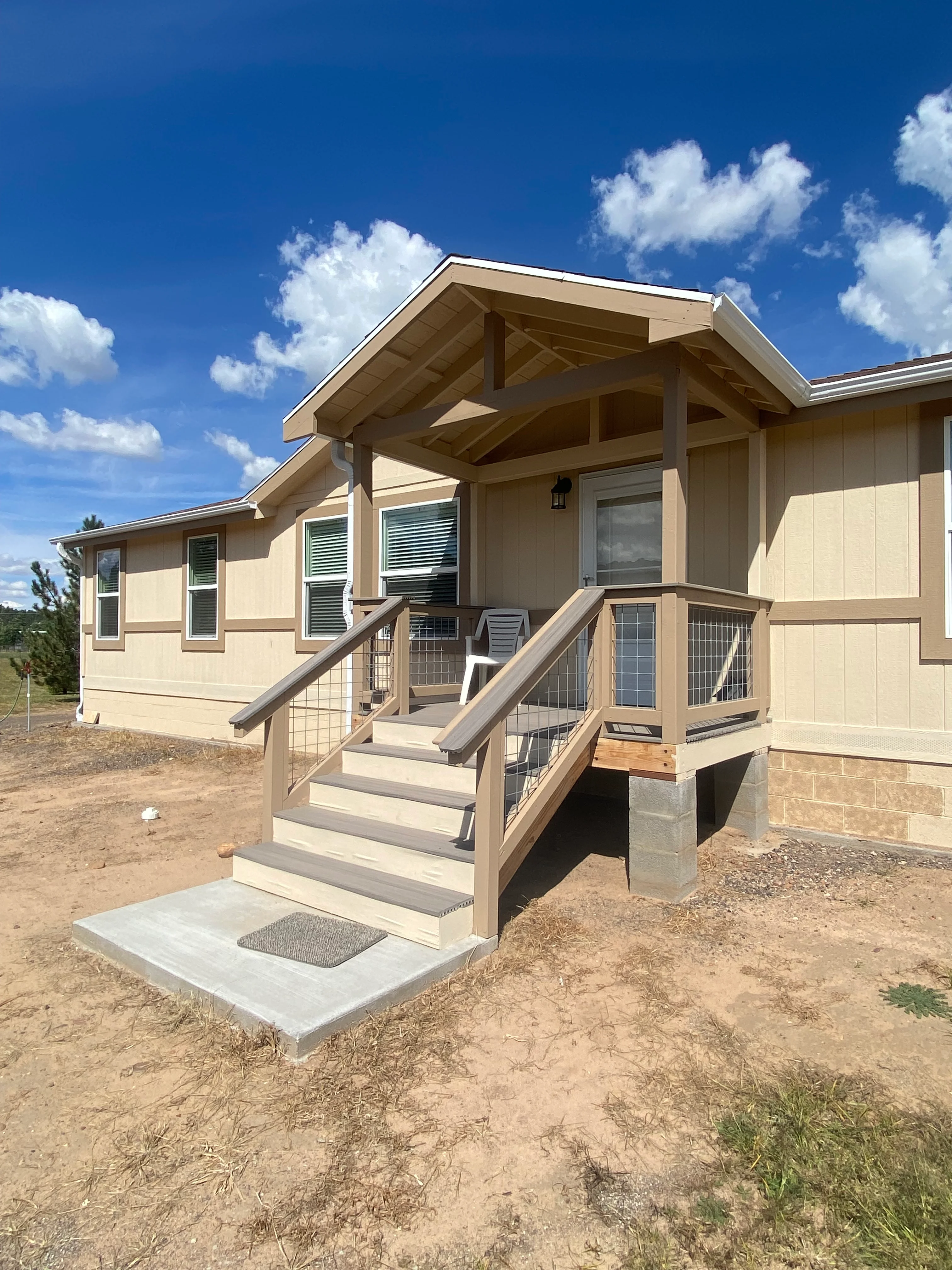 Cream and tan painted manufactured home exterior with covered porch, metal railings, and trim work