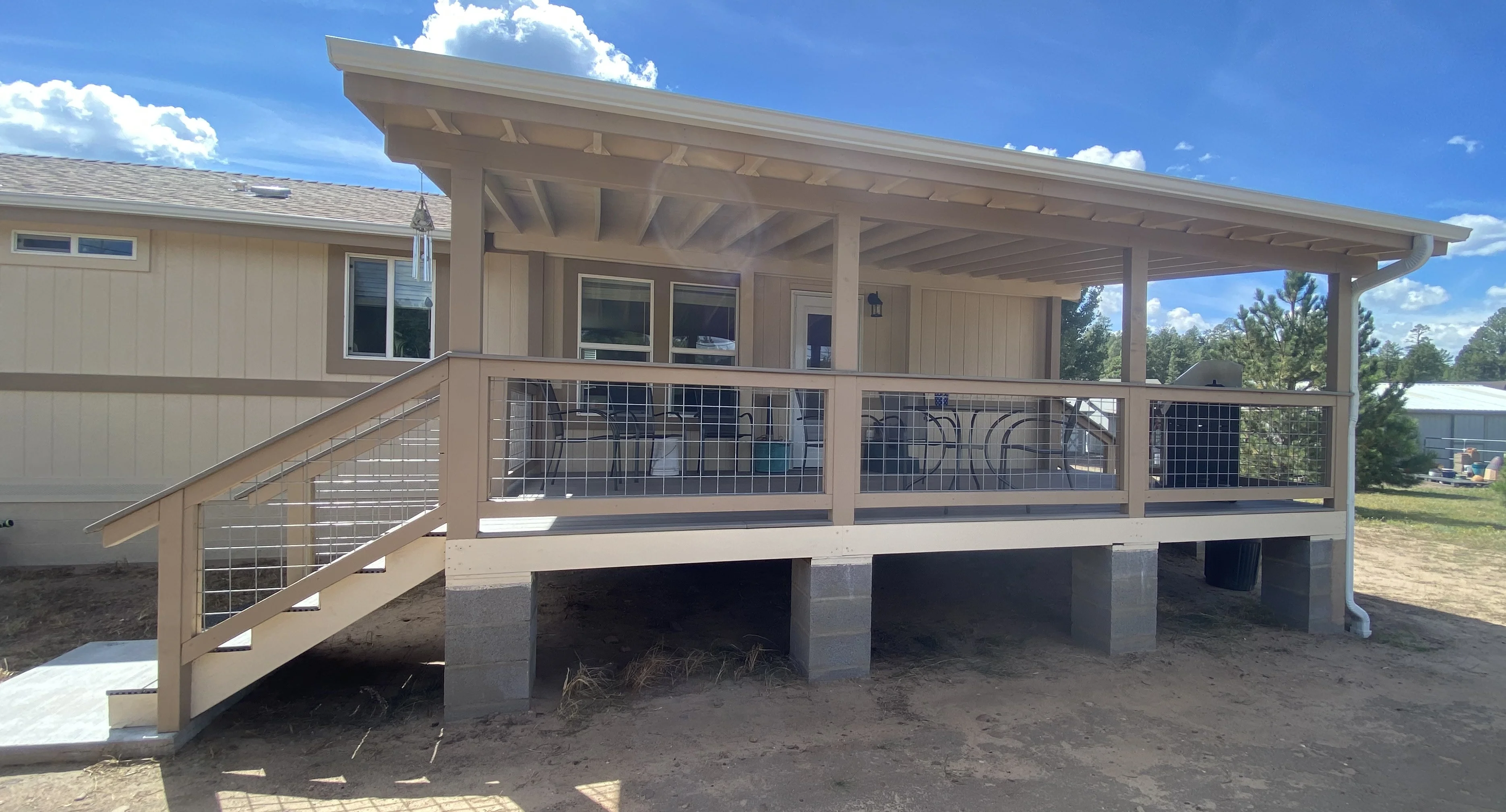 Tan painted elevated home with covered porch, metal railing, and exposed beam ceiling