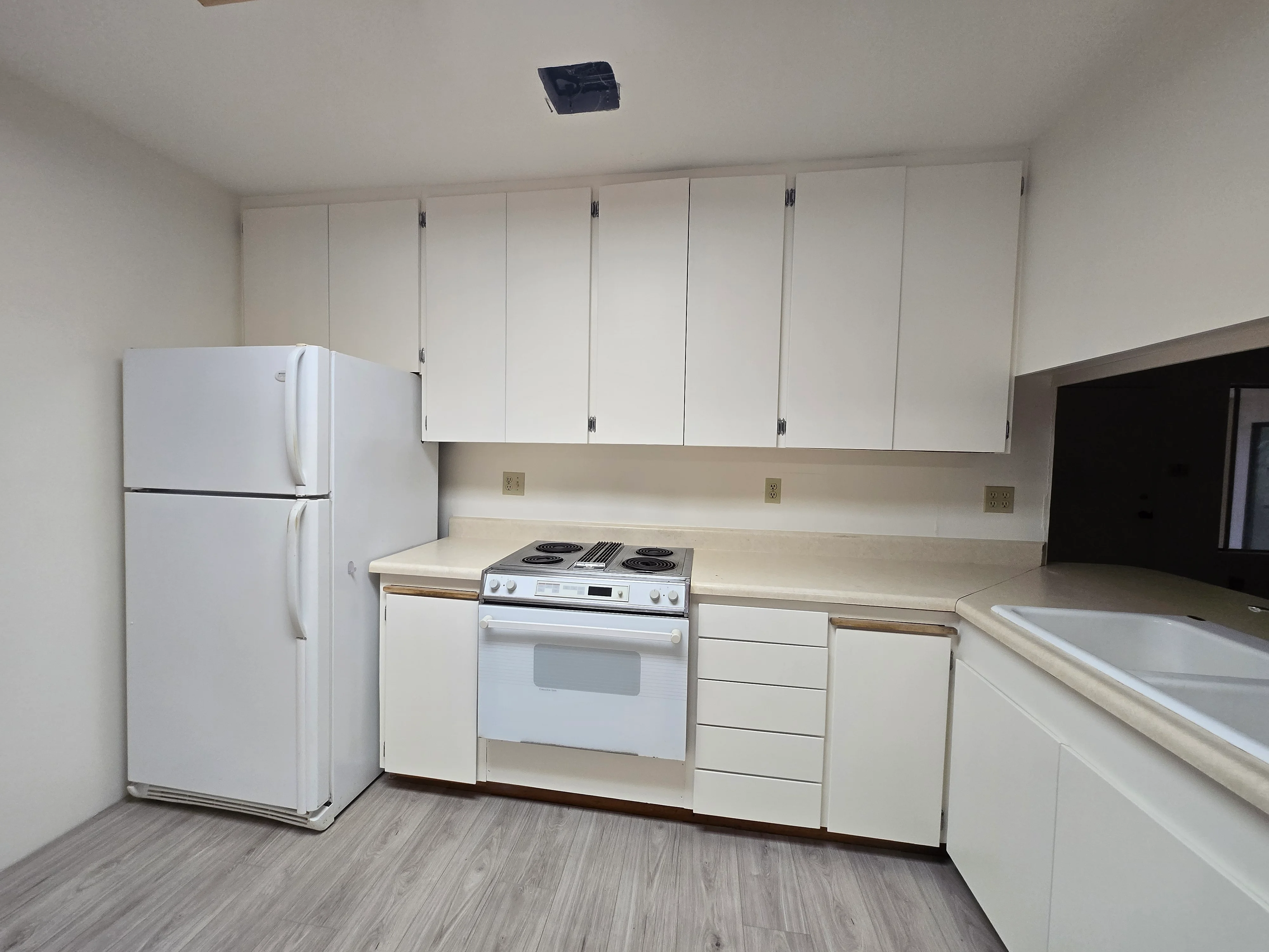 White painted kitchen cabinets with hardware, cream countertops, and stainless steel appliances