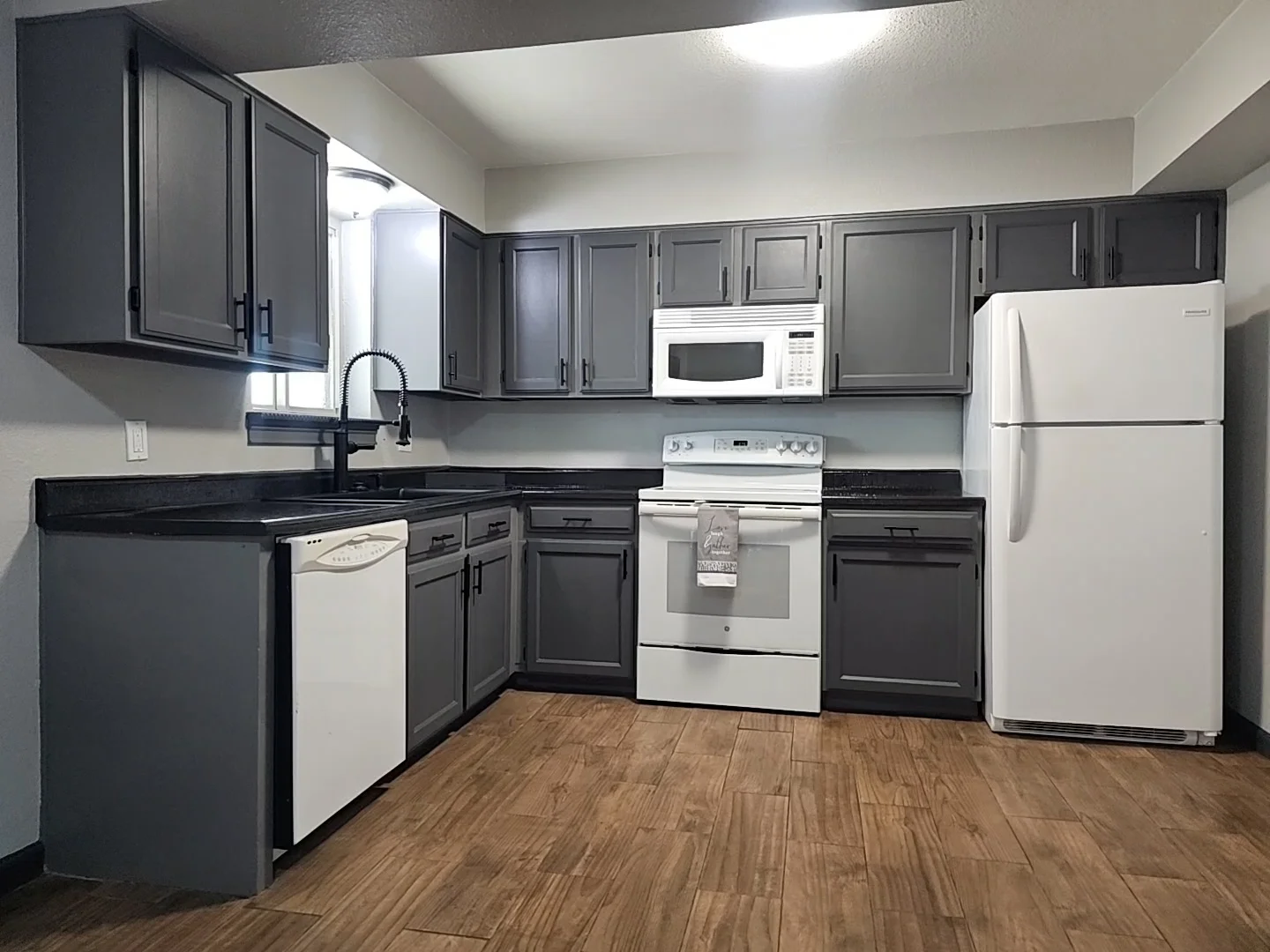 Charcoal gray painted kitchen cabinets with black granite countertops and wood flooring