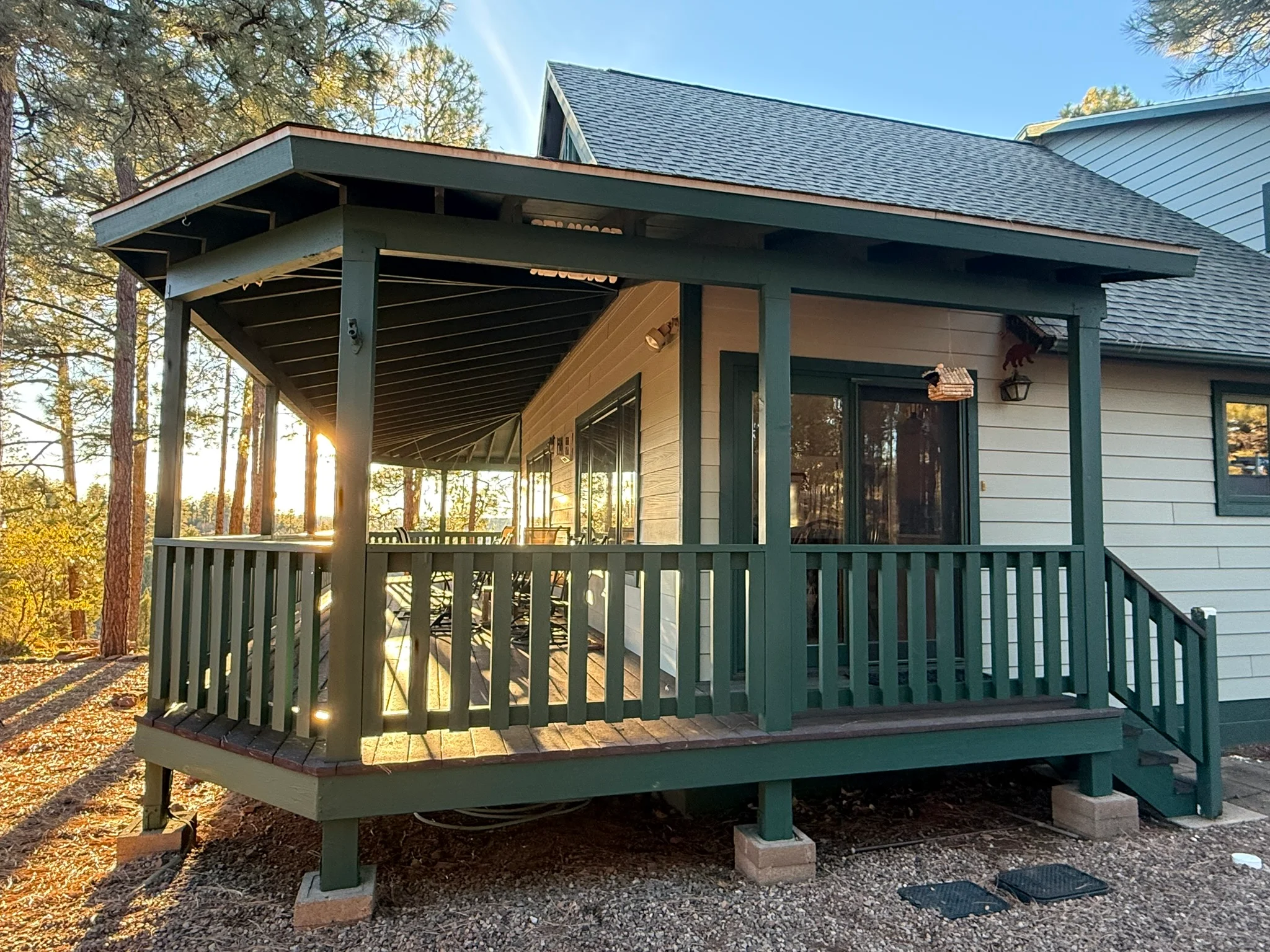 Green painted porch columns, railings, and house trim with white horizontal siding and large windows